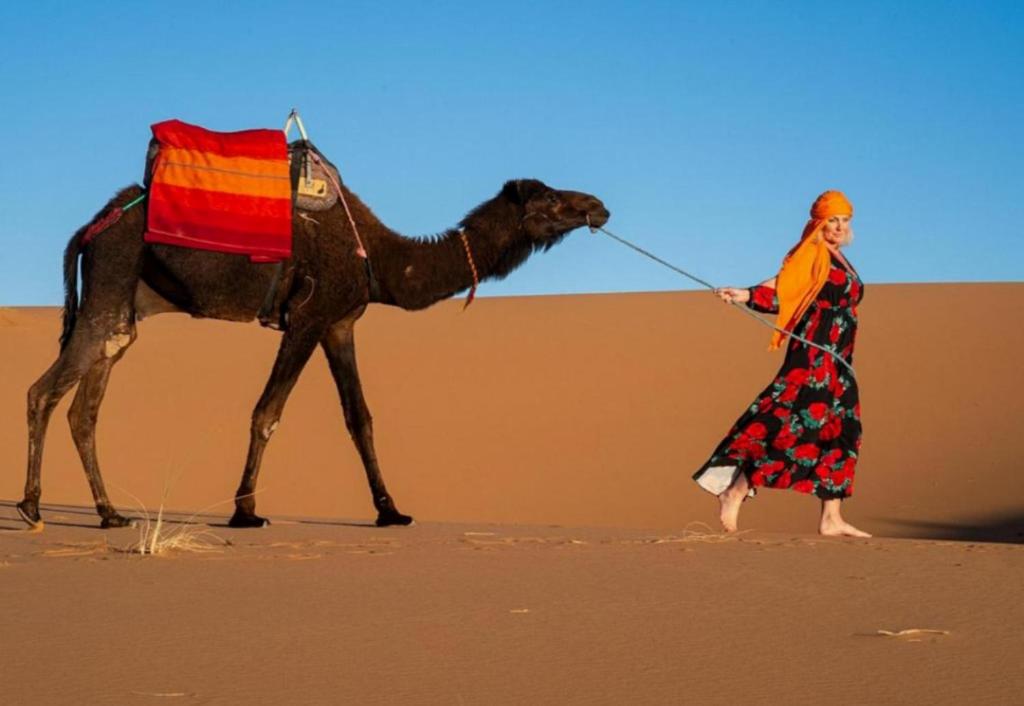 a woman walking a camel in the desert at Merzouga Stars Luxury Camp in Merzouga