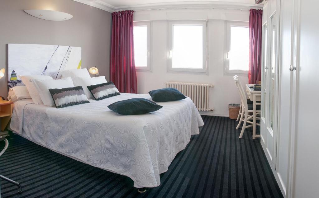 a bedroom with a white bed with pillows on it at Logis Hotel Du Casino Restaurant Le Mathelia in Vierville-sur-Mer