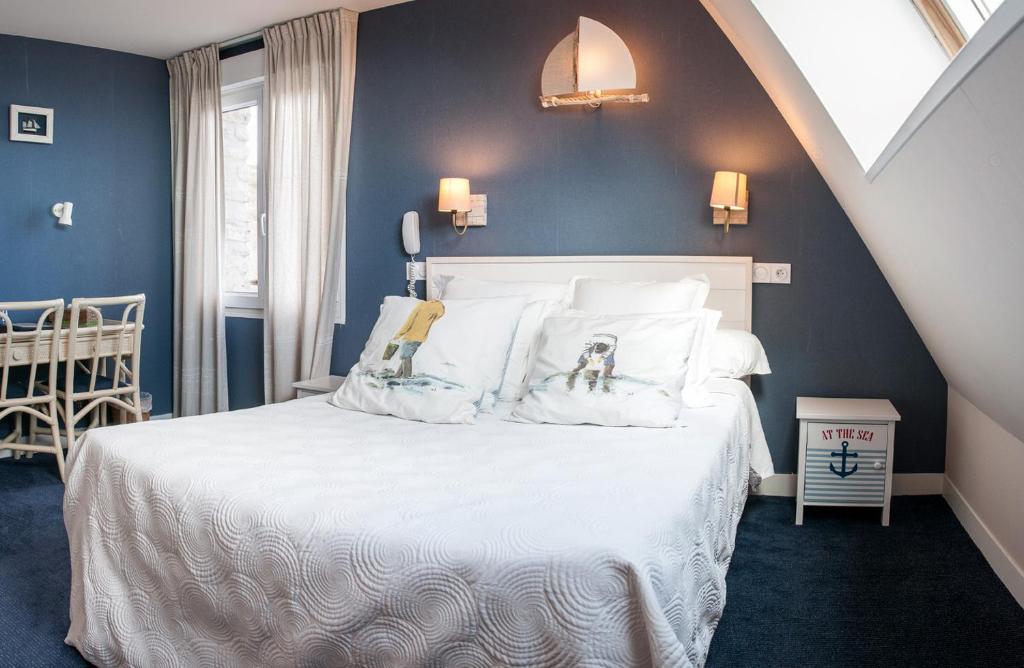 a bedroom with a white bed with blue walls at Logis Hotel Du Casino Restaurant Le Mathelia in Vierville-sur-Mer