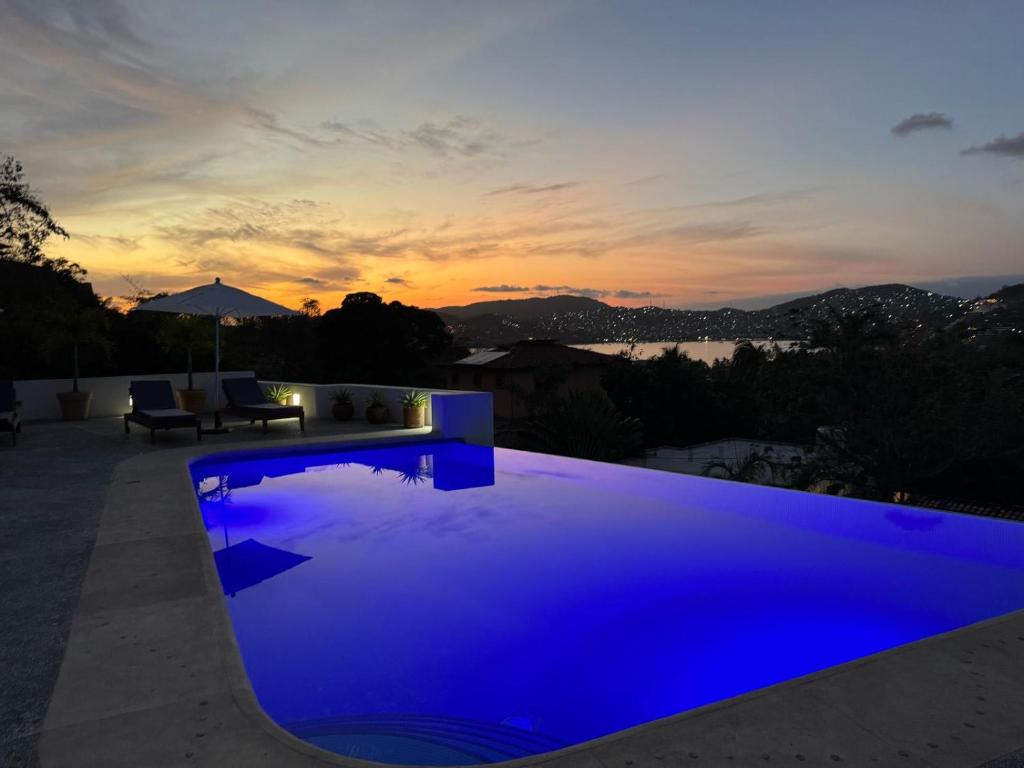 une piscine bleue avec un coucher de soleil en arrière-plan dans l'établissement El Tular 002 2 bedroom villa 7 mins walk from La Ropa beach, à Zihuatanejo