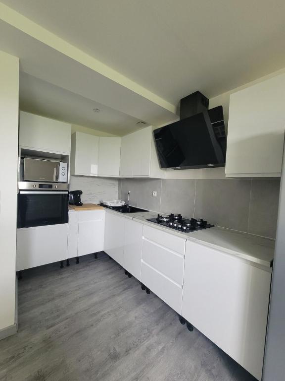 une cuisine avec des armoires blanches et des appareils noirs dans l'établissement Maison calme et moderne, à Engenville
