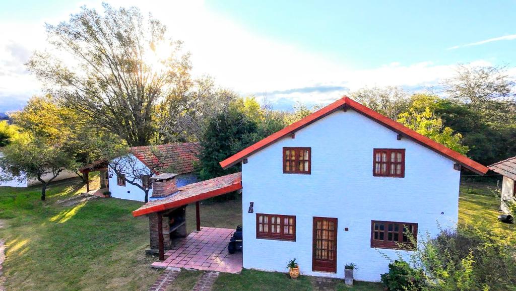 ein weißes Haus mit einem roten Dach auf einem Feld in der Unterkunft Lomas de Belgrano Oficial cabaña 1 in Villa General Belgrano