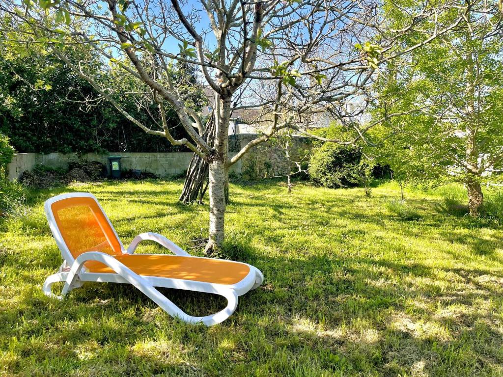 une chaise orange et blanche assise dans l'herbe à côté d'un arbre dans l'établissement Maison T5 atypique rénovée PMR – Centre de Locmiquélic – Classée 2* - FR-1-479-228, à Locmiquélic