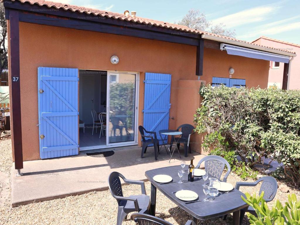 d'une terrasse avec des portes bleues, des tables et des chaises. dans l'établissement Pavillon 3 Pièces, Terrasse, Narbonne Plage - FR-1-229B-110, à Narbonne