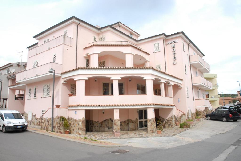 różowy budynek z samochodami zaparkowanymi przed nim w obiekcie Riccio Hotel w mieście La Maddalena