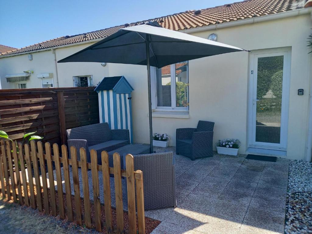 een patio met een parasol, stoelen en een hek bij Maison proche du centre ville in Pornic