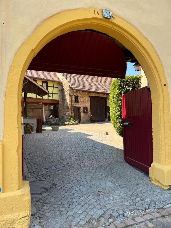 une arche menant à un bâtiment avec une porte rouge dans l'établissement Chambre maison vigneronne - Val du Patre, à Orschwihr