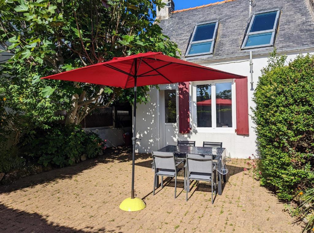 une table avec un parapluie rouge devant une maison dans l'établissement VIEUX PASSAGE, Maison avec cour privée à 150 m du PORT et de la PLAGE, à Plouhinec