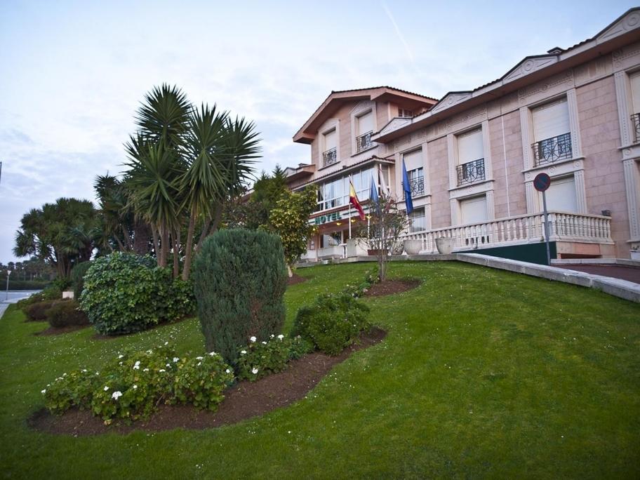 a building with a green yard with plants and trees at Hotel Begoña Park in Gijón
