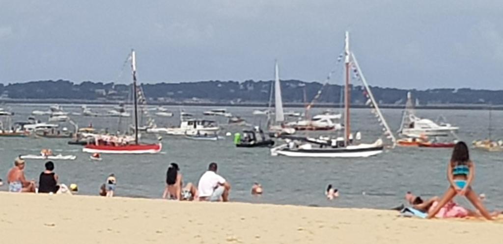 un groupe de personnes sur une plage avec des bateaux dans l'eau dans l'établissement Residence grand voile avec vue bassin, à Arcachon