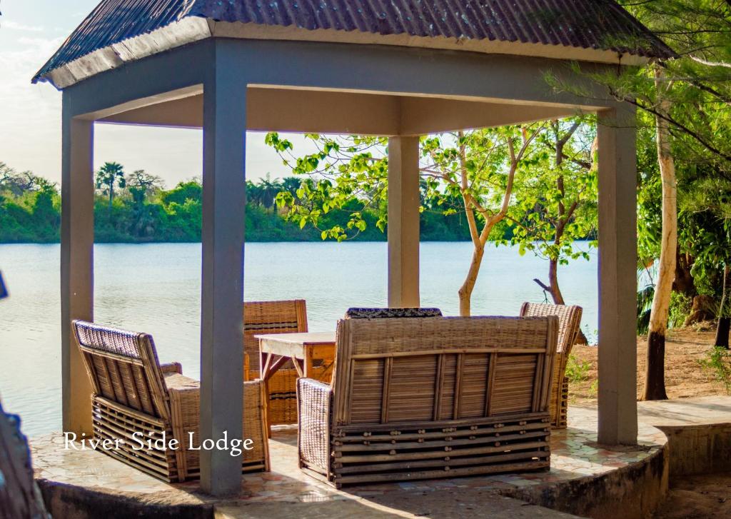 a gazebo with chairs and a table and water at Riverside Lodge Bansang in Bansang