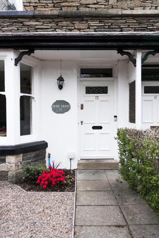 a white house with a white door and red flowers at Denecrest Guest House in Windermere