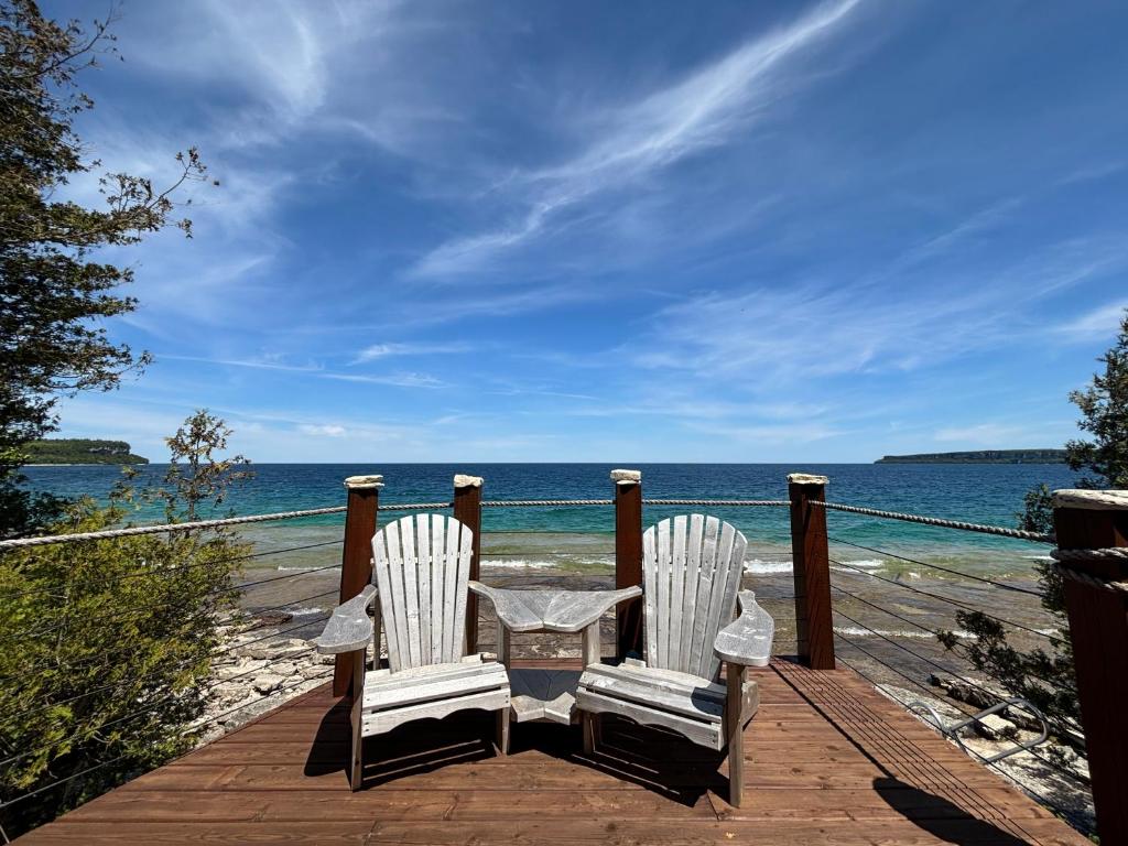 two white chairs sitting on a wooden deck overlooking the ocean at Beeshore Lakehouse Waterfront Bliss & Comfort in Lions Head