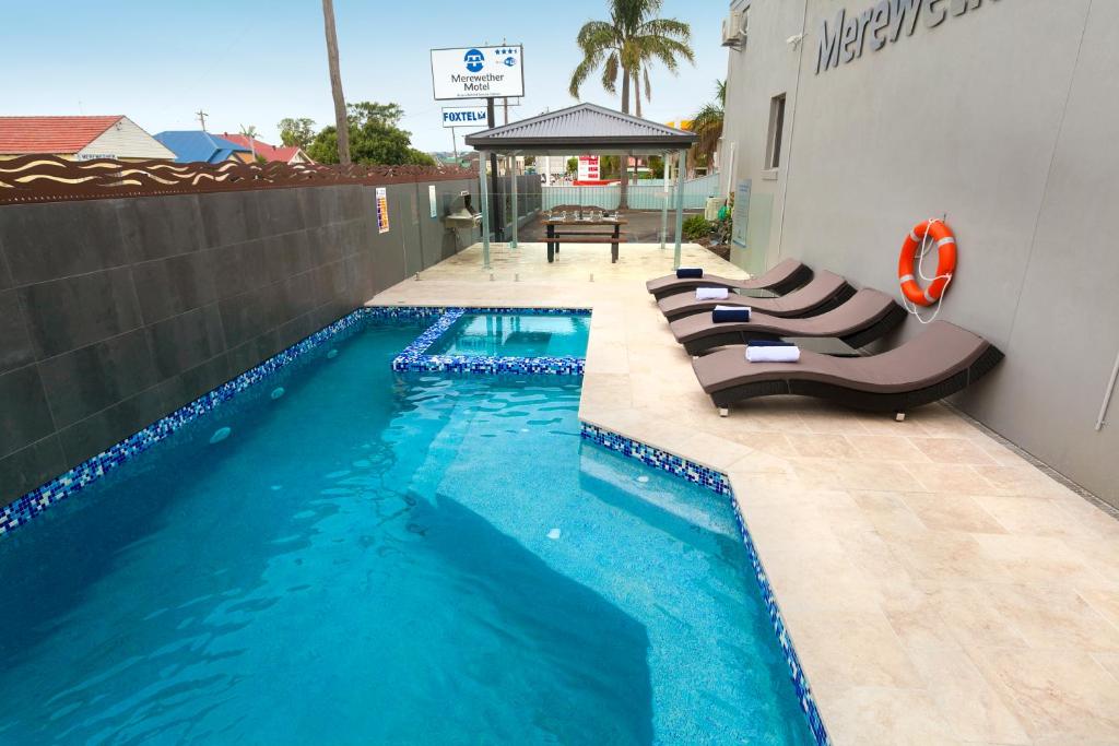 a swimming pool with lounge chairs next to a building at Merewether Motel in Newcastle