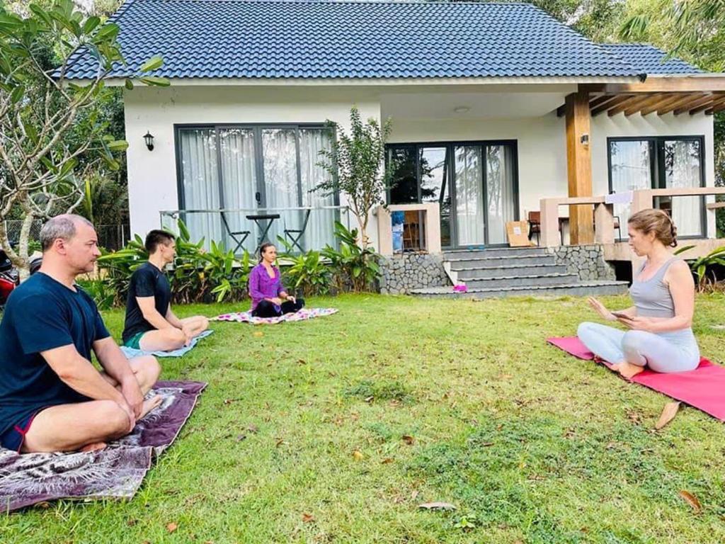 a group of people sitting in the grass in front of a house at Baisao Villa in Phú Quốc