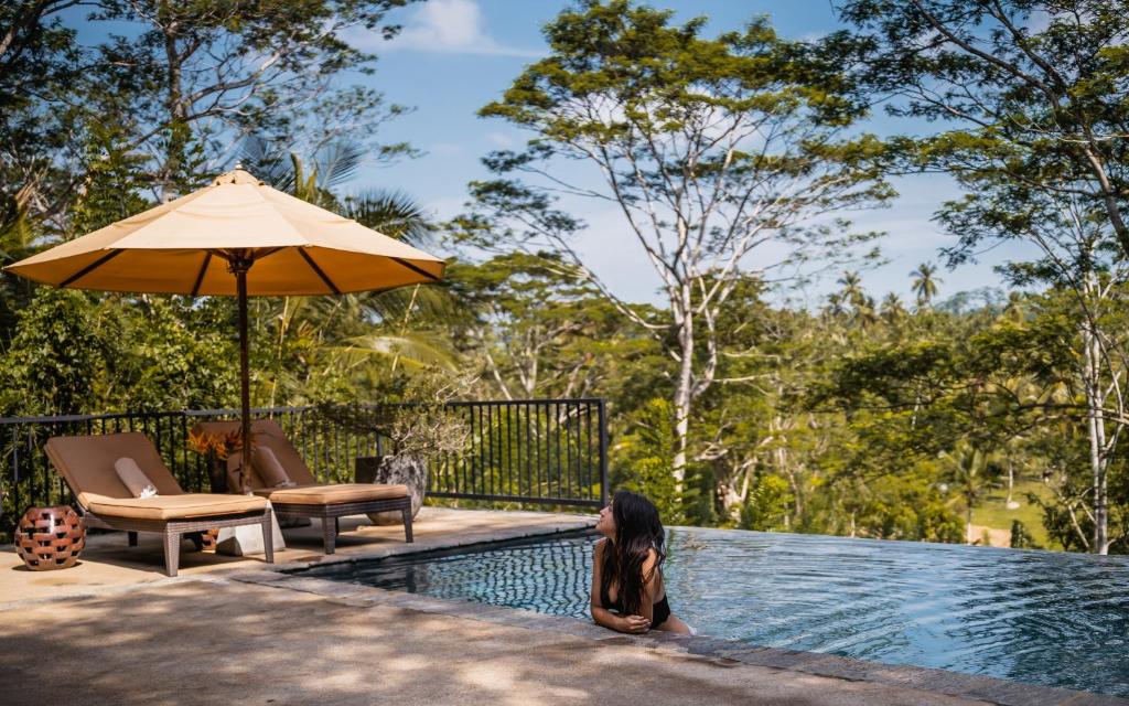 a woman sitting next to a swimming pool with an umbrella at Kahanda Kanda in Koggala