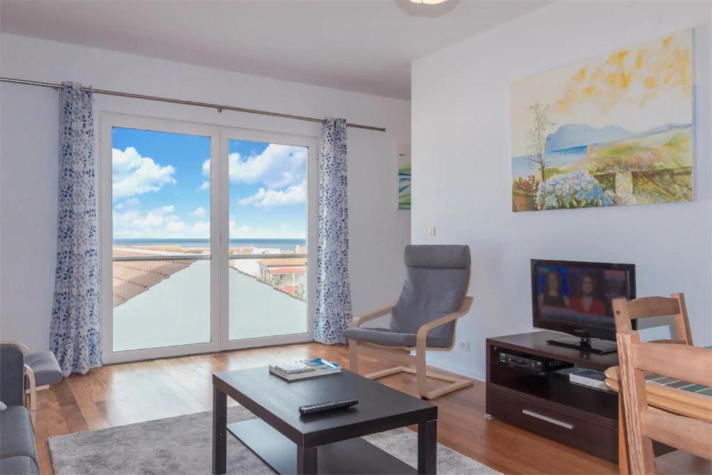 a living room with a chair and a television and a window at Downtown Praia da Vitória AL in Praia da Vitória