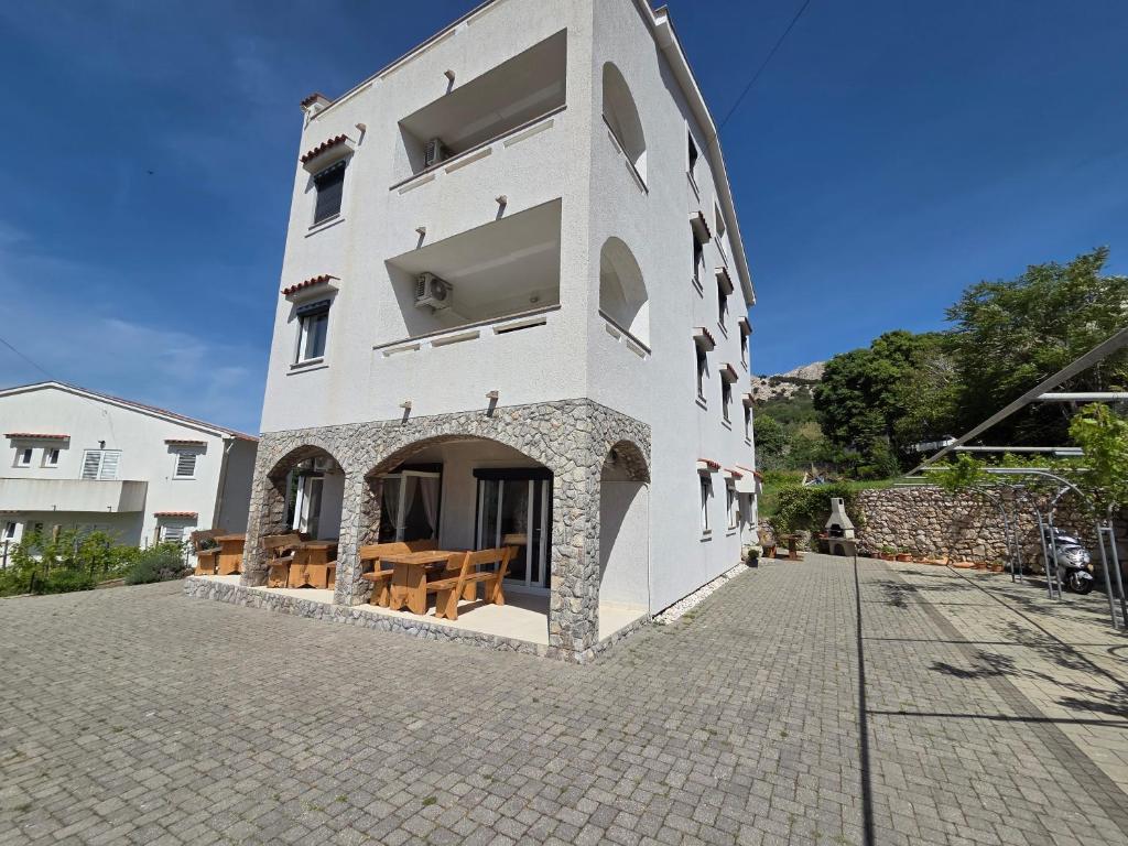 biały budynek ze stołami i ławkami na ulicy w obiekcie Apartments Leticia I w Bašce