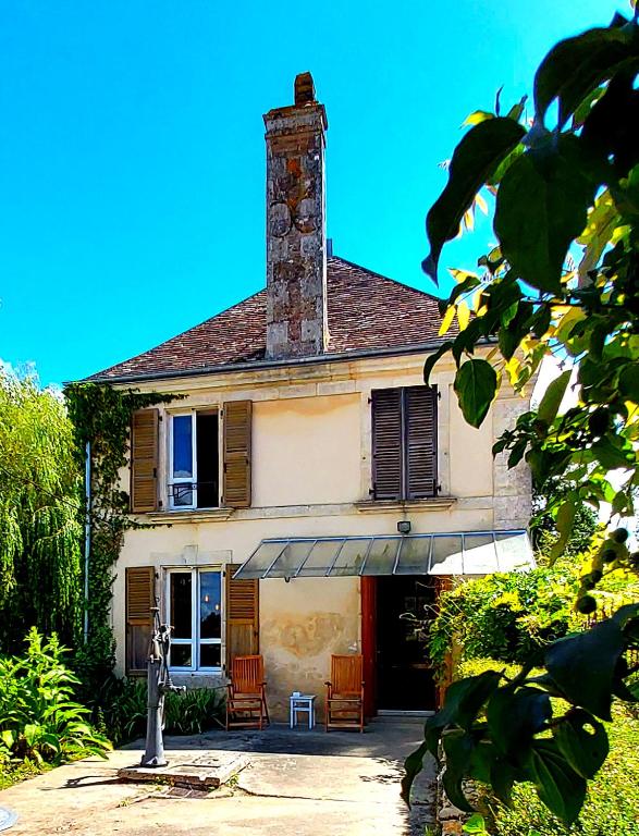 une maison avec une cheminée et des chaises devant dans l'établissement Le Moulin en Route kamer rose en grijs, badkamer en suite, à Blèves