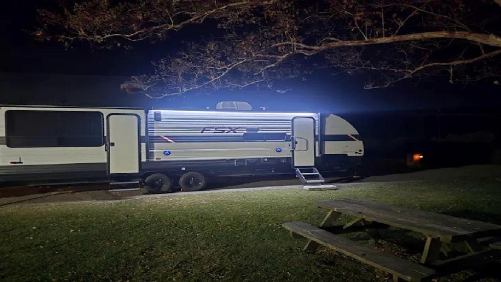 un rimorchio blu e bianco parcheggiato in un parco di notte di Cozy Equipped Camper With Picnic Space, Pool and BBQ in Virginia a Diggs