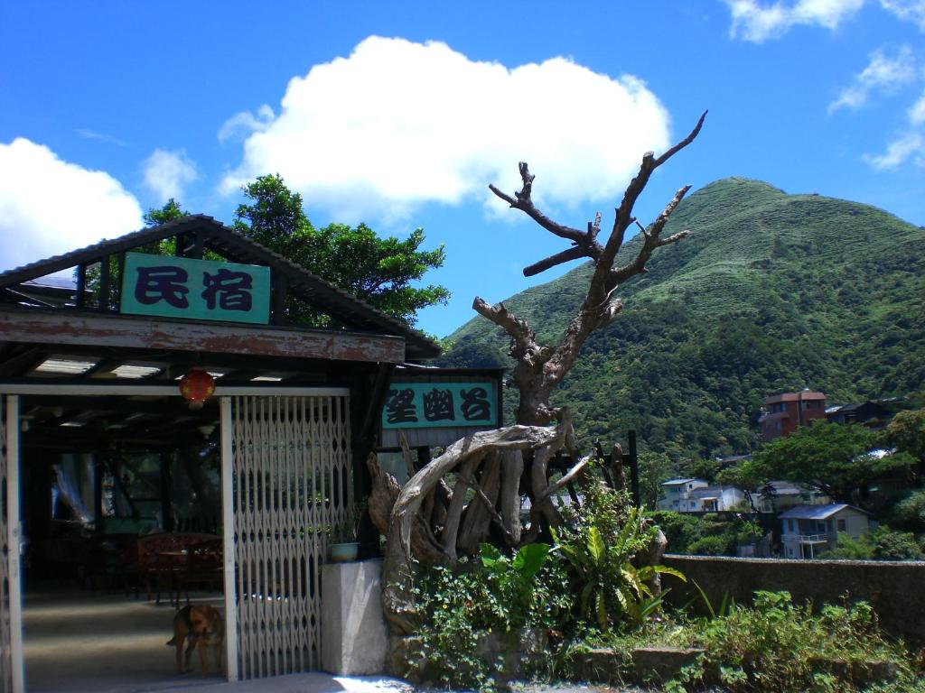 a building with a tree in front of a mountain at Wangyuku B&B in Jiufen