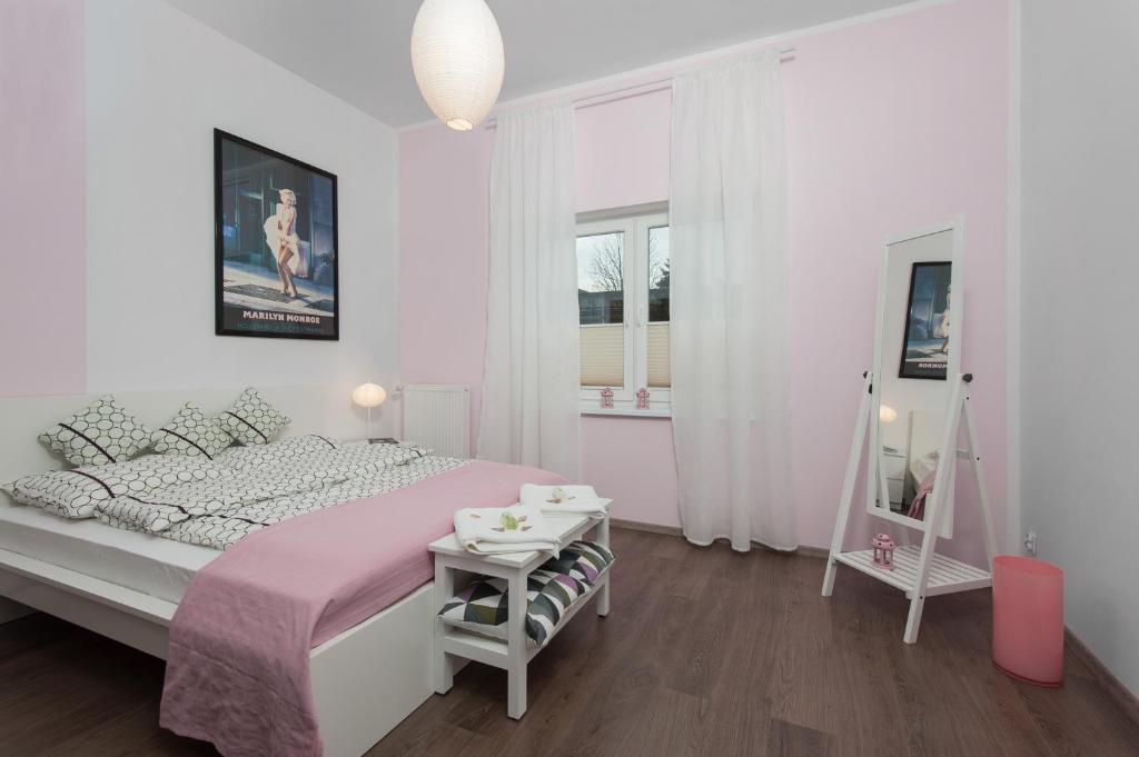 a white bedroom with a pink bed and a table at Iva Mare in Darłówko