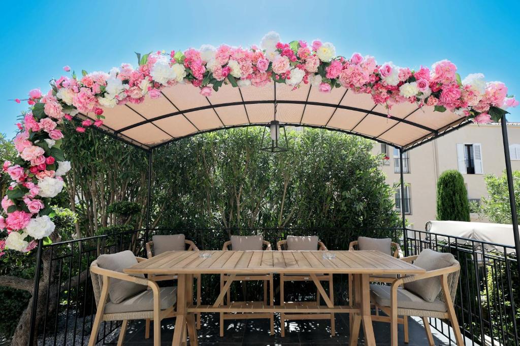 a wooden table with a large arch with pink and white flowers at Hôtel L'Abbaye in Calvi