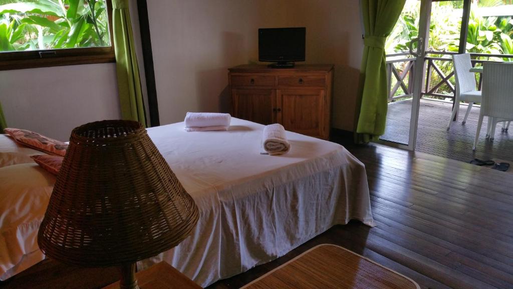 a bedroom with a bed with a white blanket and a television at Pension de famille HITI MOANA VILLA in Papara