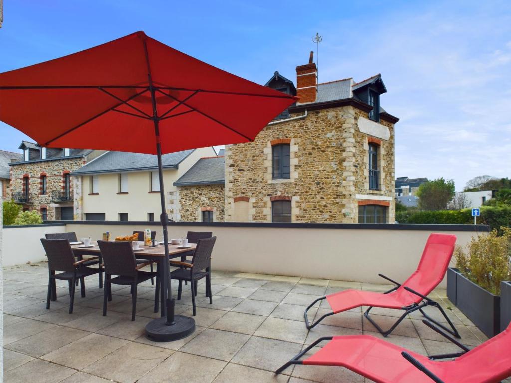 a patio with a table and chairs and a red umbrella at 50m de la plage - terrasse - 3 adultes et 3 enfants in Pléneuf-Val-André