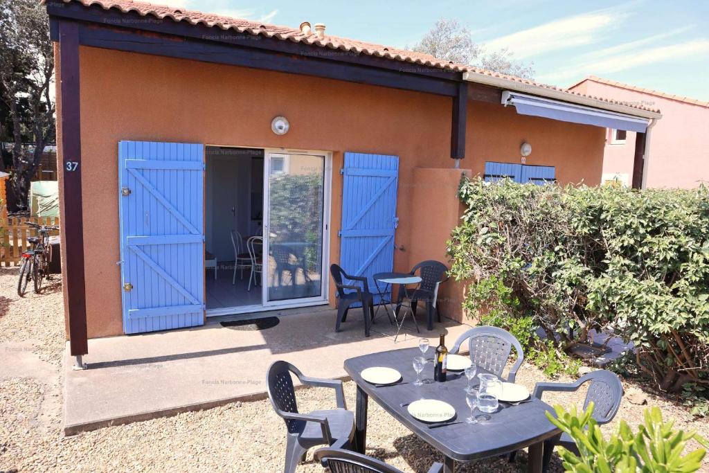 d'une terrasse avec des portes bleues, une table et des chaises. dans l'établissement NP020-037 Pavillon 3 pièces mezzanine Narbonne Plage, à Narbonne-Plage