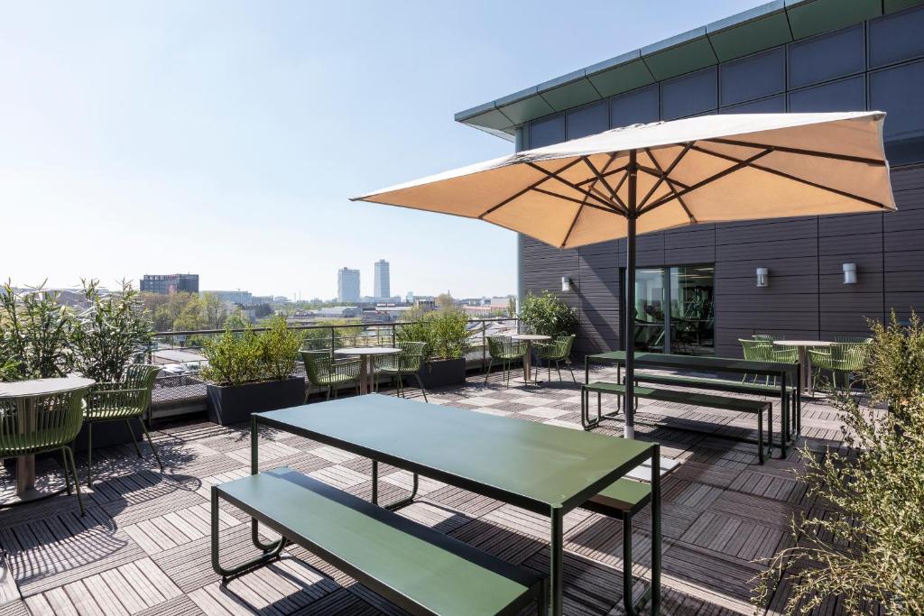 un patio avec tables, chaises et un parasol dans l'établissement Novotel Paris Saint Denis Stade Basilique, à Saint-Denis