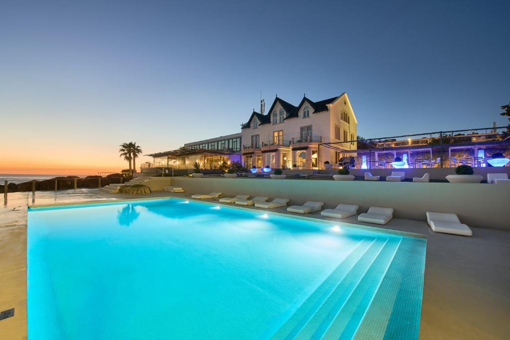 a swimming pool in front of a house and the ocean at Farol Hotel in Cascais