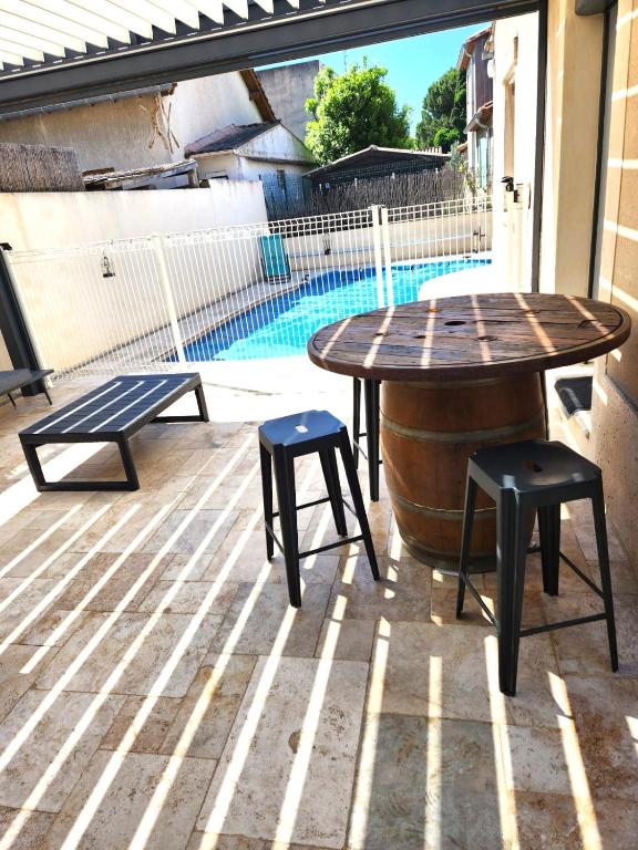 une table et deux tabourets sur une terrasse avec piscine dans l'établissement Maison de vacances - St Joseph, à Beaucaire