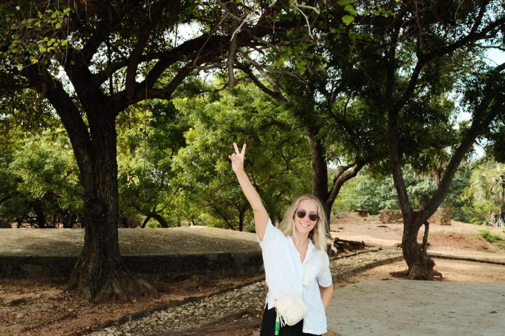eine Frau in weißem Hemd und Sonnenbrille steht vor Bäumen in der Unterkunft Koala Backpackers in Trincomalee