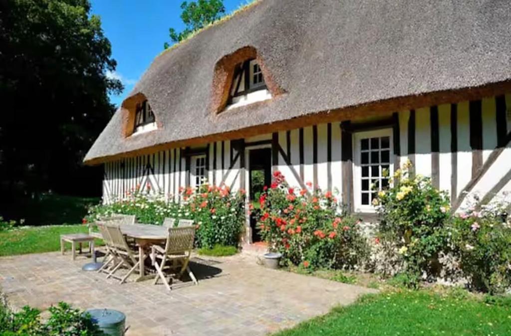une maison au toit de chaume avec une table et des chaises dans l'établissement Chaumière du Val, à Triqueville