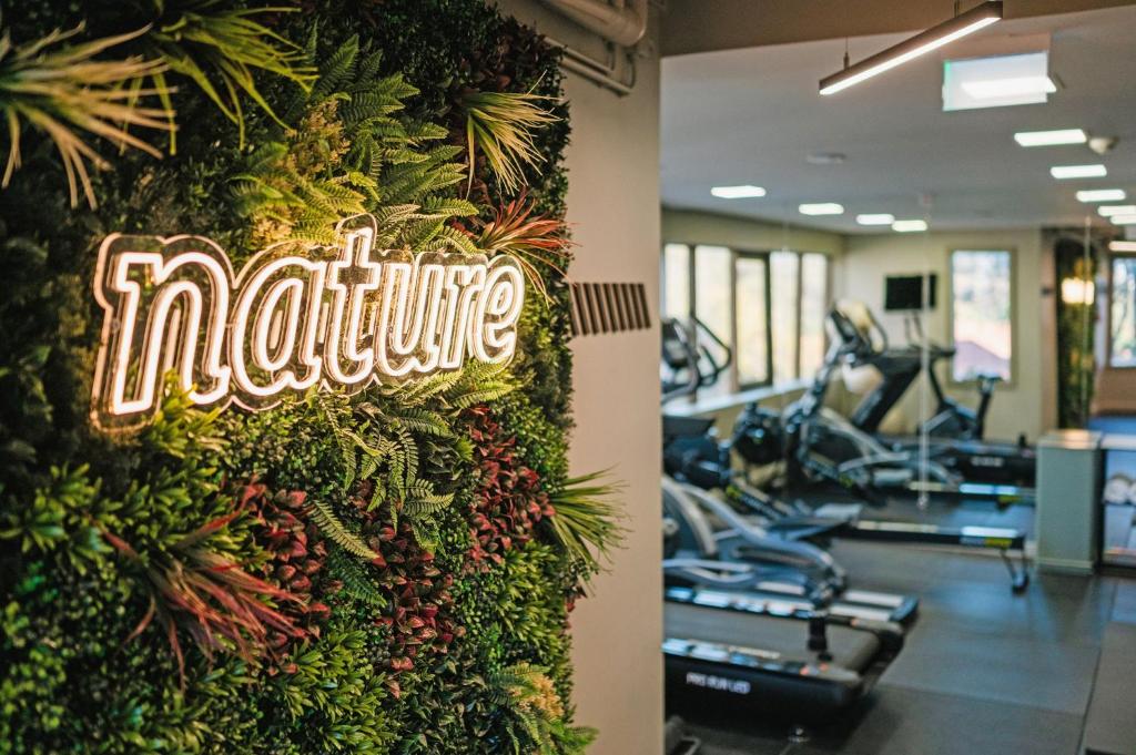 A hotel gym with cardio machines visible beyond a greenery feature wall.