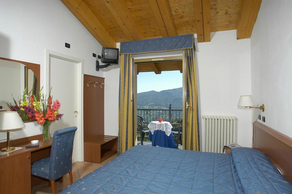 um quarto com uma cama azul, uma secretária e uma janela em Hotel Al Poggio em Sestola