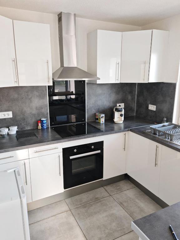 une cuisine avec des armoires blanches et un four noir dans l'établissement Appartement Bartenheim, à Bartenheim
