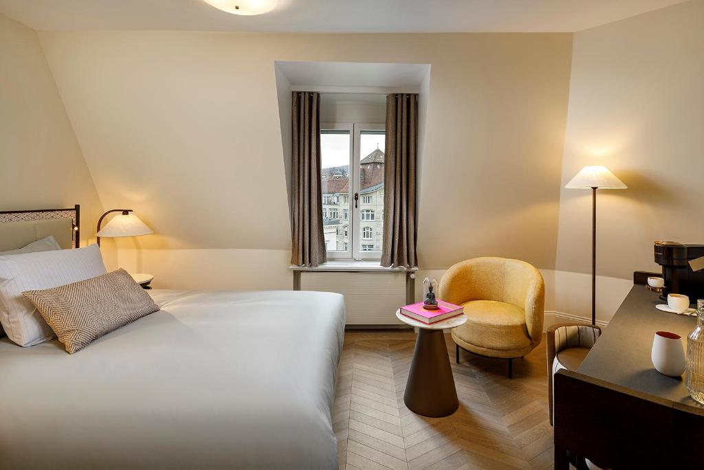 a hotel room with a bed and a chair and a window at Small Luxury Hotel Ambassador Zurich in Zürich