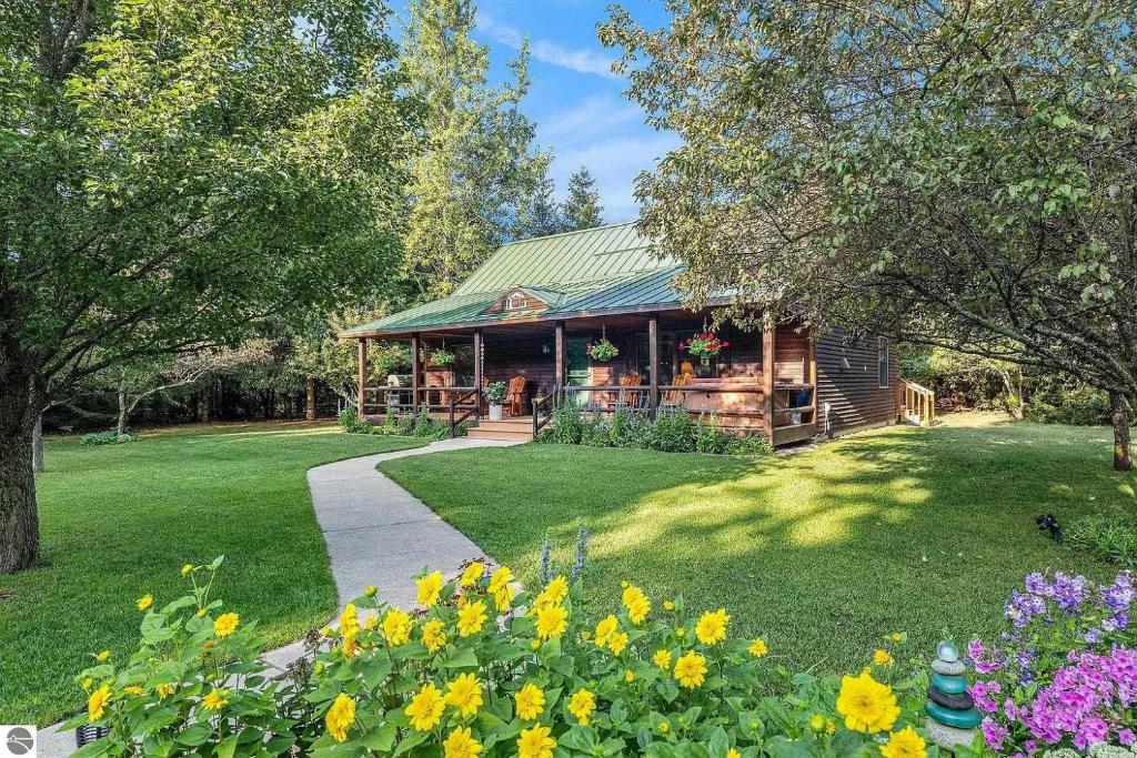 a log cabin with flowers in the yard at Majestic Escapes Hot Tub Firepit Deck Large Yard in Lake Ann