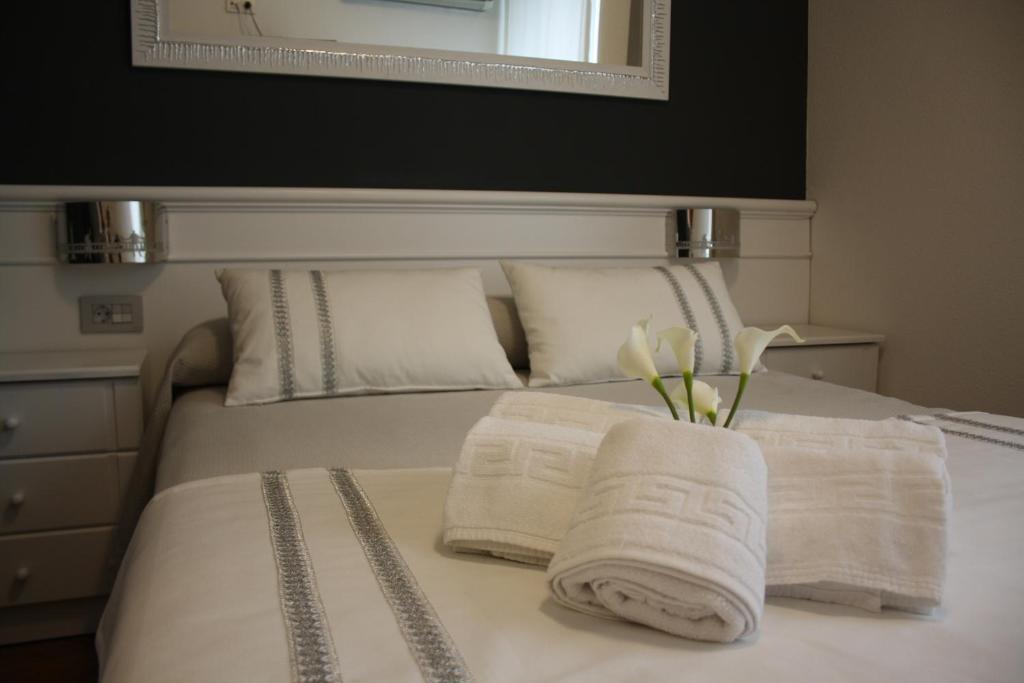 a white bed with two towels and a vase of flowers at Hotel Herreros in Castellón de la Plana
