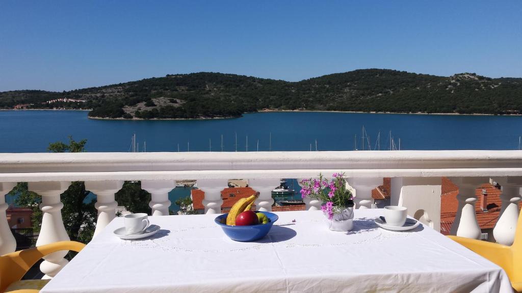 een witte tafel met een fruitschaal op een balkon bij Apartments Petranić in Tisno