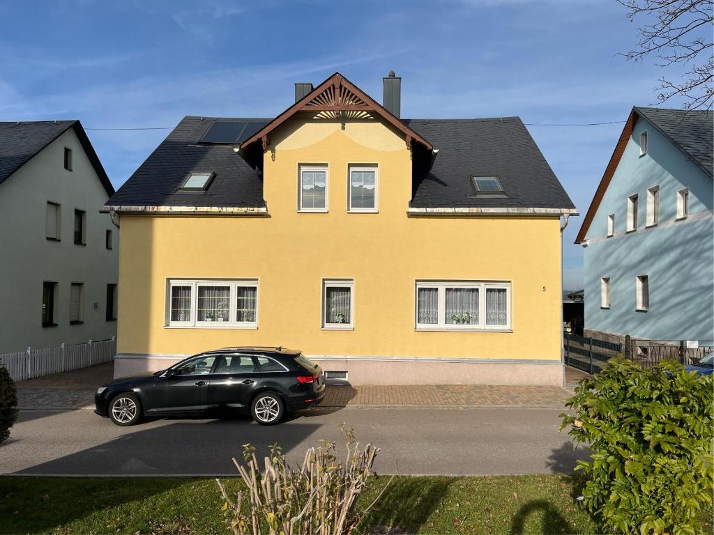 a black car parked in front of a yellow house at Ferienwohnung Hagert - Ankommen und Wohlfühlen in Eibenstock