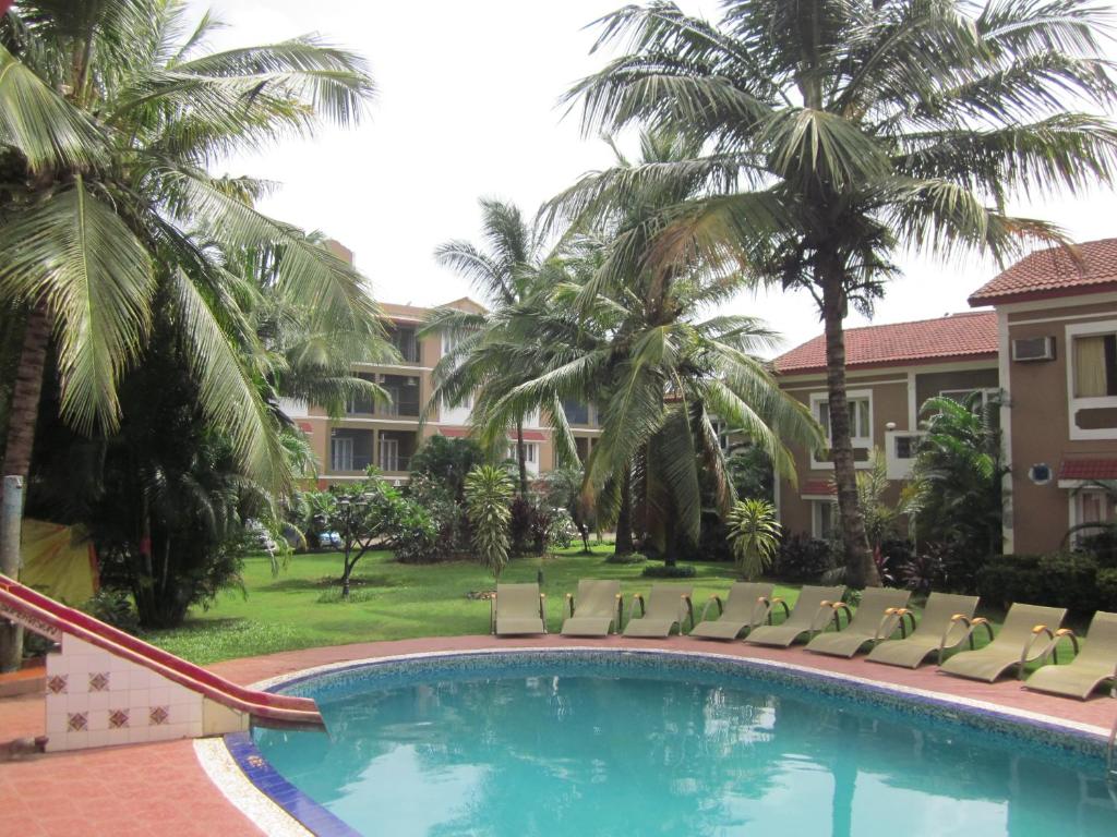 a pool with chairs and palm trees in front of a building at FF-1 Apartment in Candolim