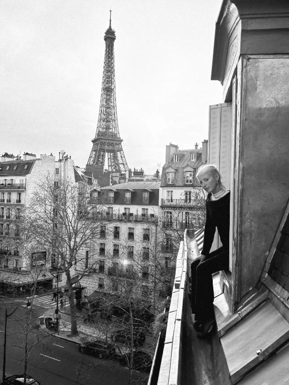 un homme assis sur le rebord d'une fenêtre avec la tour Eiffel dans l'établissement Cozy Charming Studio with breathtaking view, à Paris