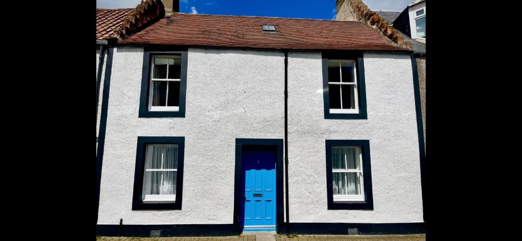 a white house with a blue door at No3 By The Sea a 5 Star Cozy Coastal Cottage in Saint Monance