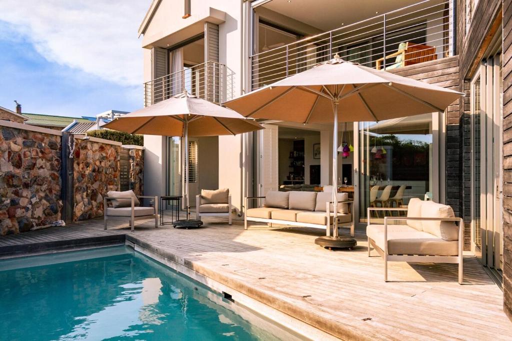 a house with a pool and two umbrellas at Coastal Cove Whale Watching Retreat in De Kelders