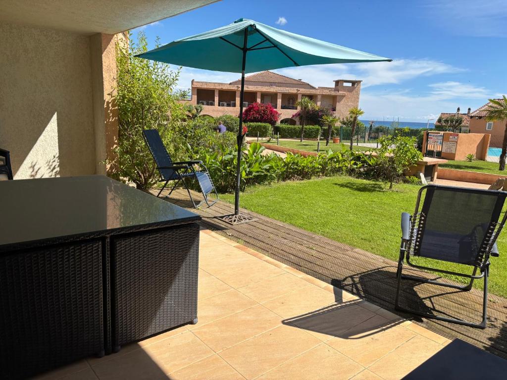 a patio with two chairs and an umbrella at PALMERAIE 220 in Sari Solenzara