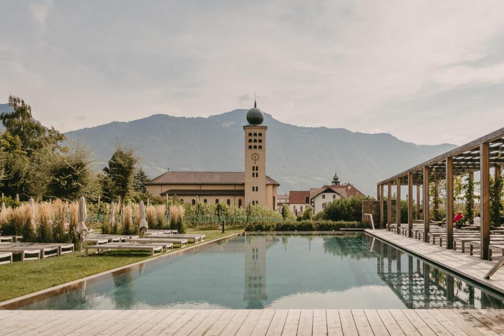 ein Gebäude mit einem Uhrturm und einem Schwimmbad in der Unterkunft Hotel Schwarzschmied, a Member of Design Hotels in Lana