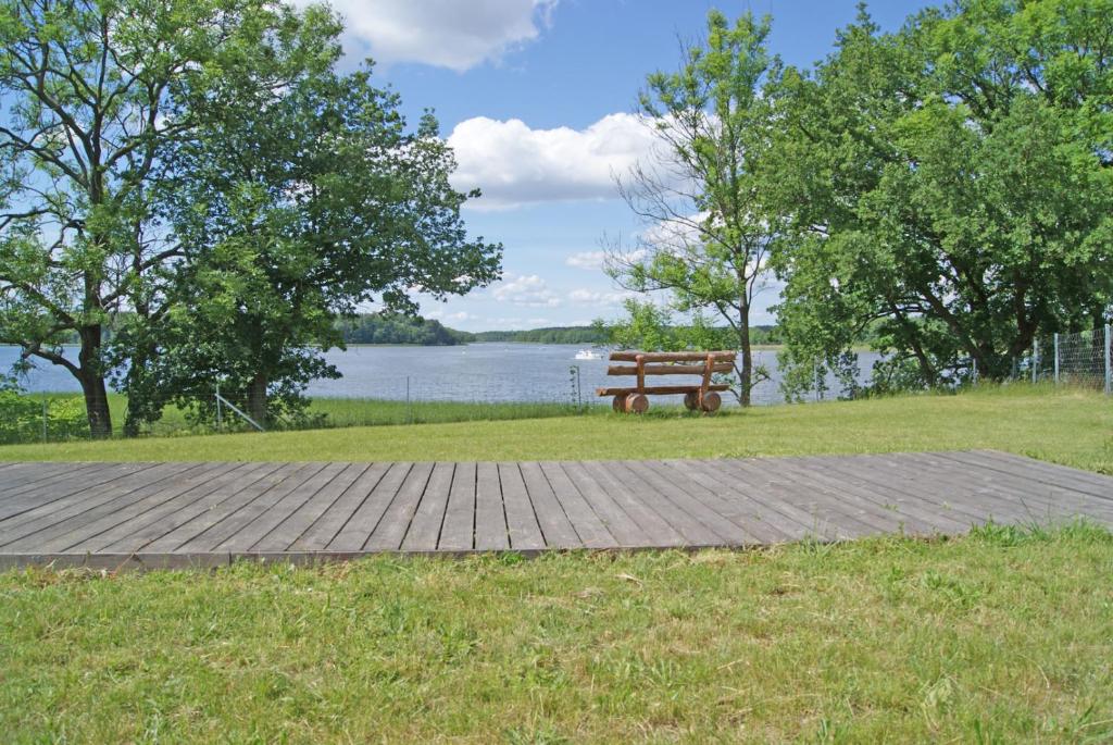 a wooden bench sitting on the grass near a lake at Ferienwohnung Vilzsee in Mirow